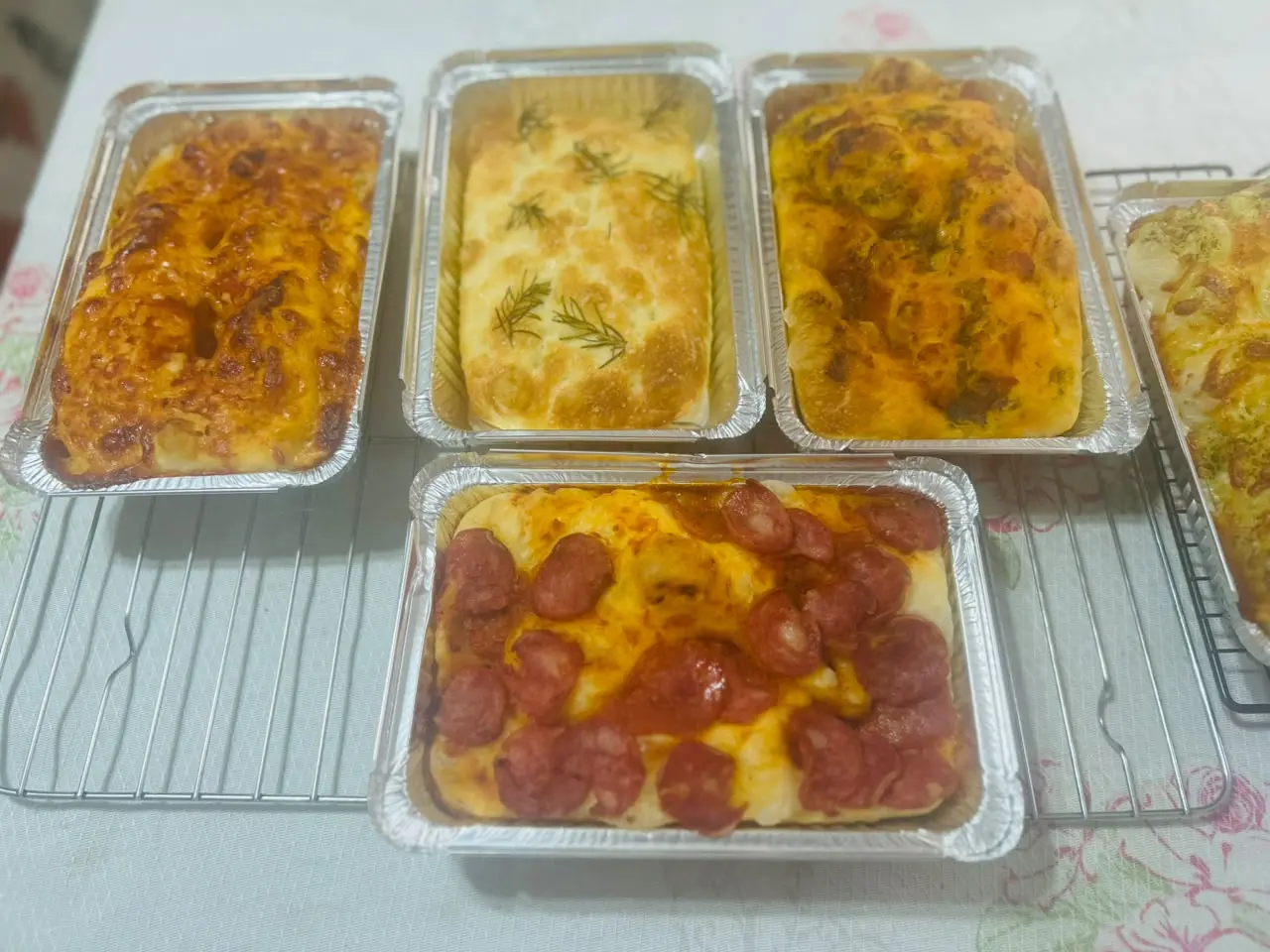 As focaccias da Sant'Anna lado a lado nas marmitas de alumínio: a clássica com ramos de alecrim, as gratinadas e a de calabresa